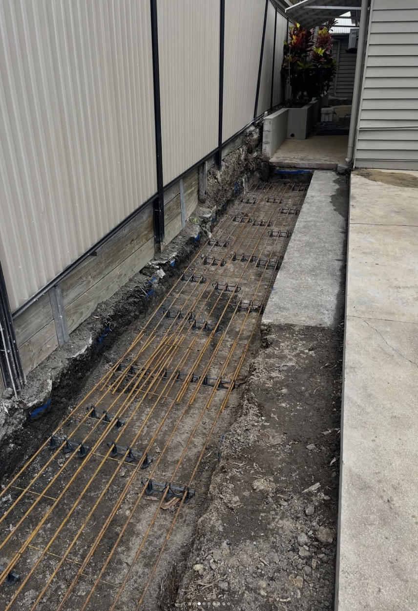 Excavated boundary wall footing with reinforcing steel beside a paved path