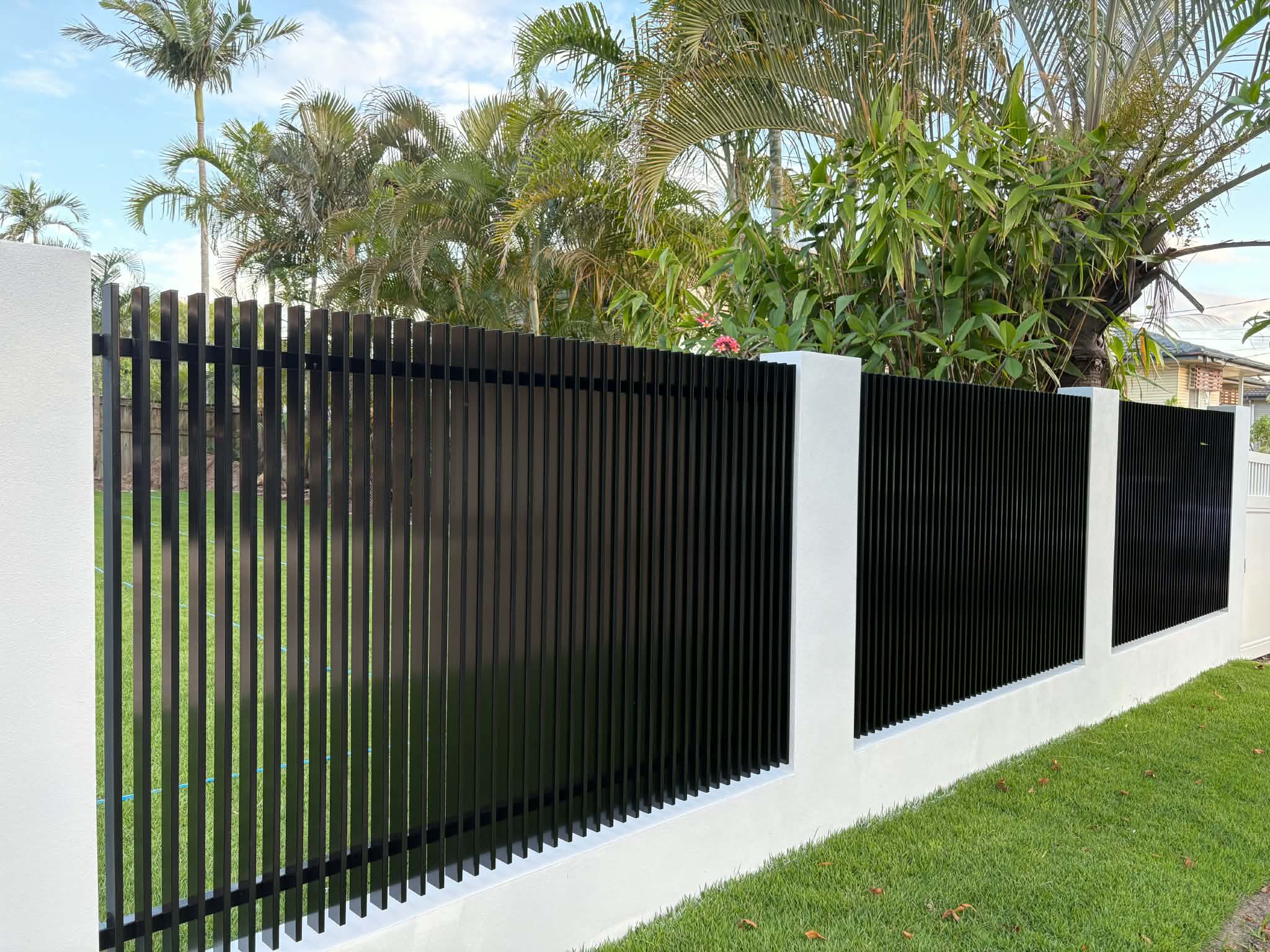 Finished black vertical-slat fence framed by white rendered block piers
