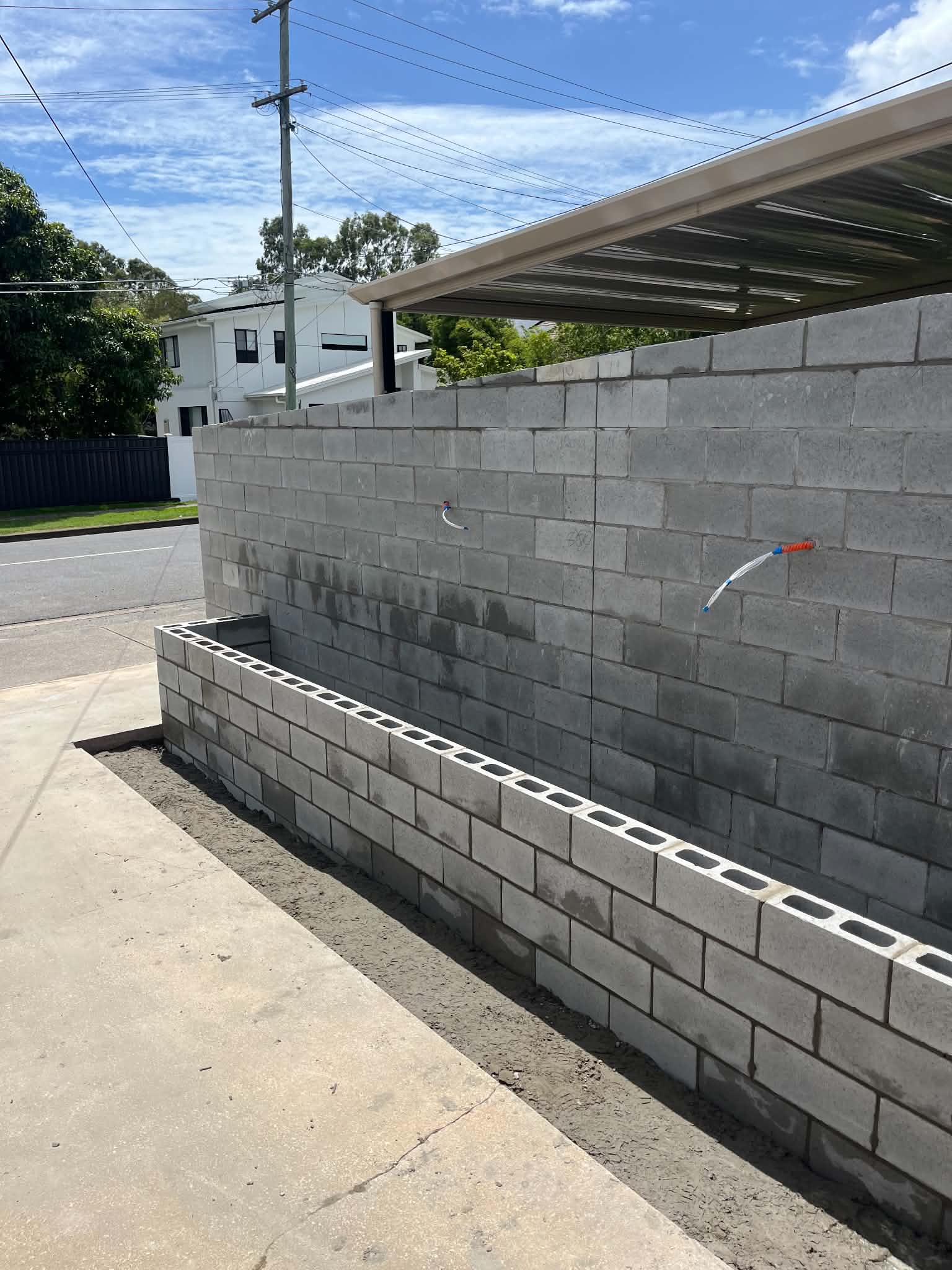 Unfinished grey block wall and raised planter beside a carport