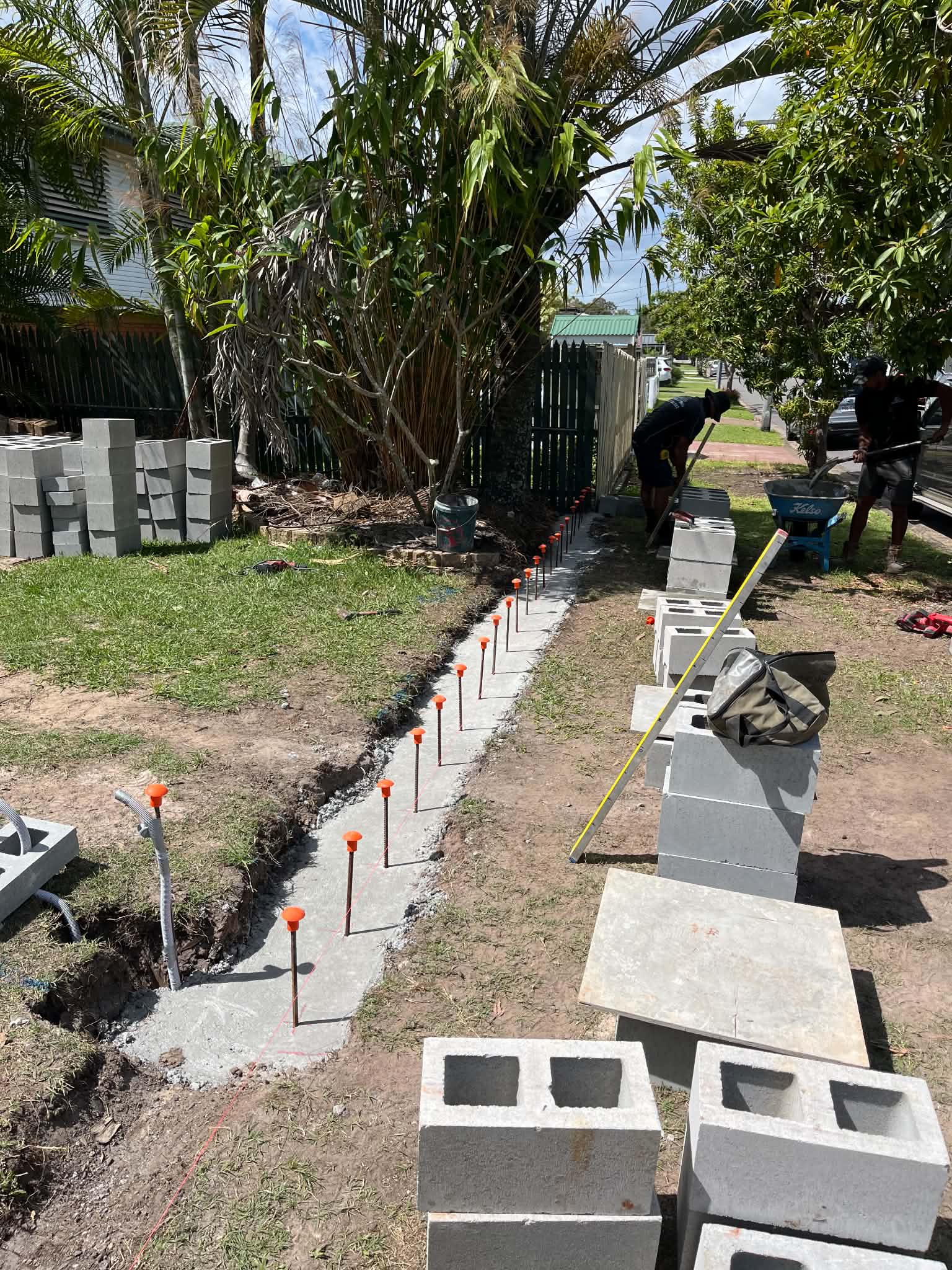 Two workers beside a long concrete footing and stacked concrete blocks