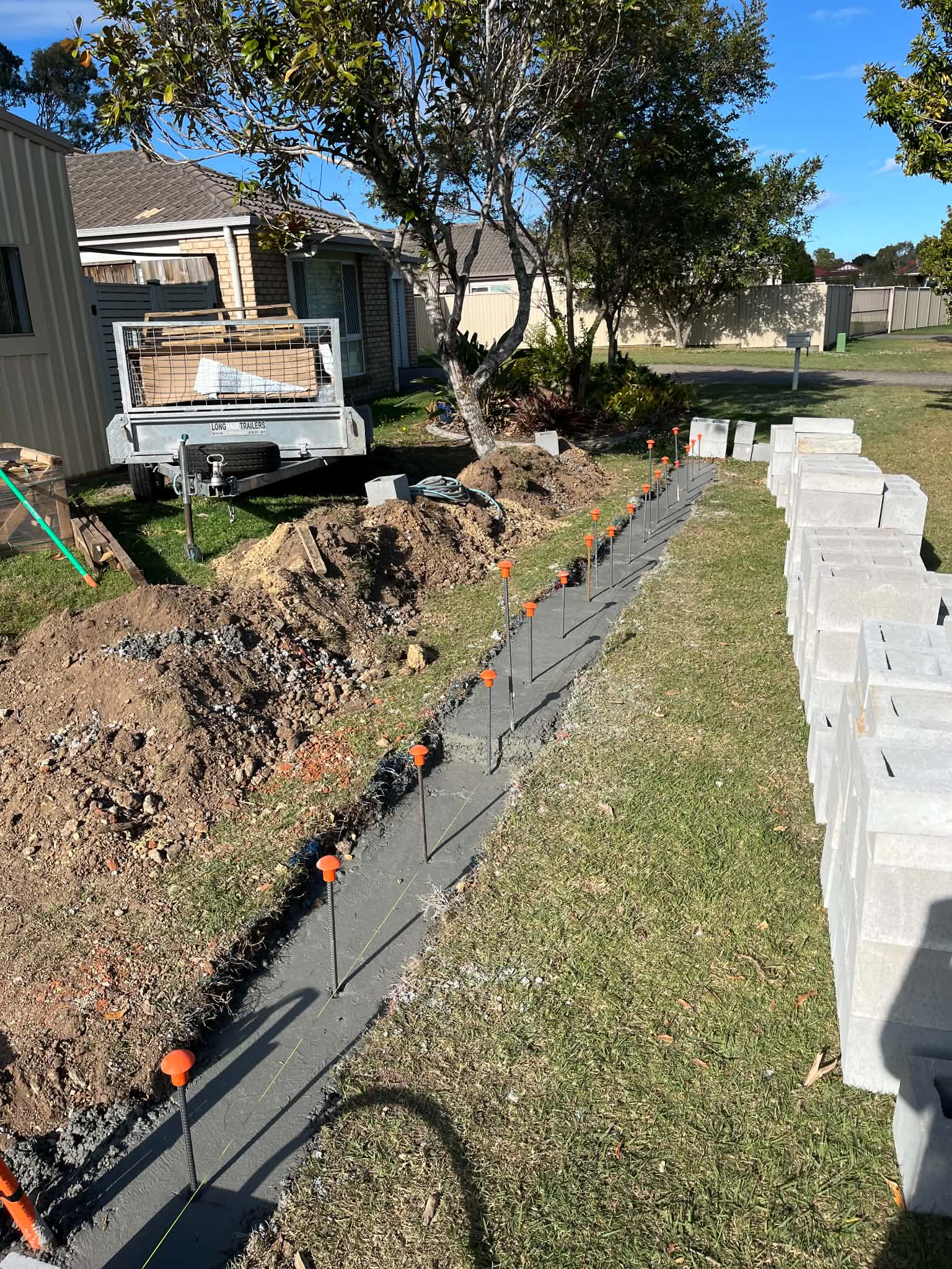 Fresh concrete footing with upright reinforcing bars and blocks stacked beside it