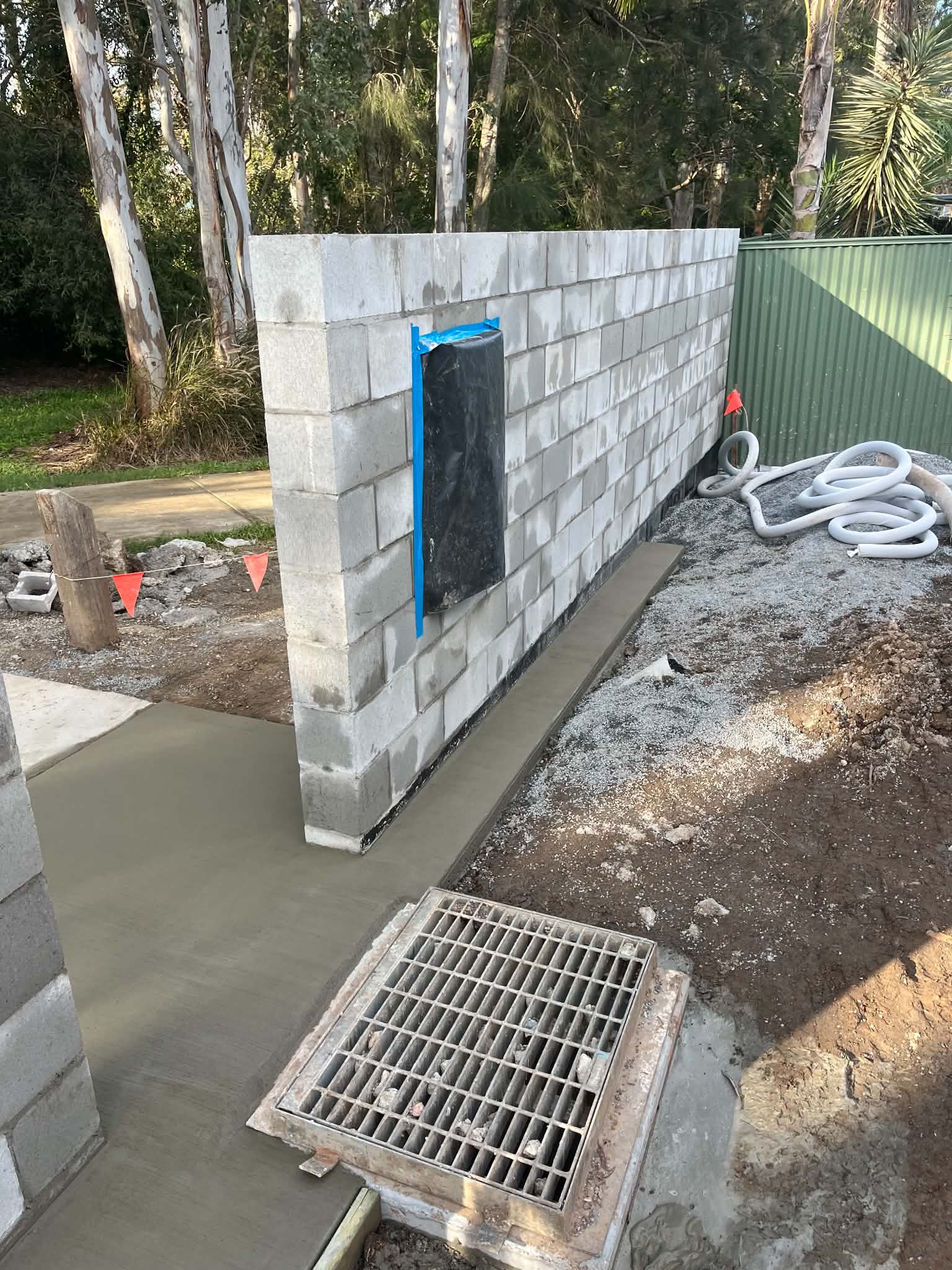Unfinished front block fence with protected mailbox opening beside a path