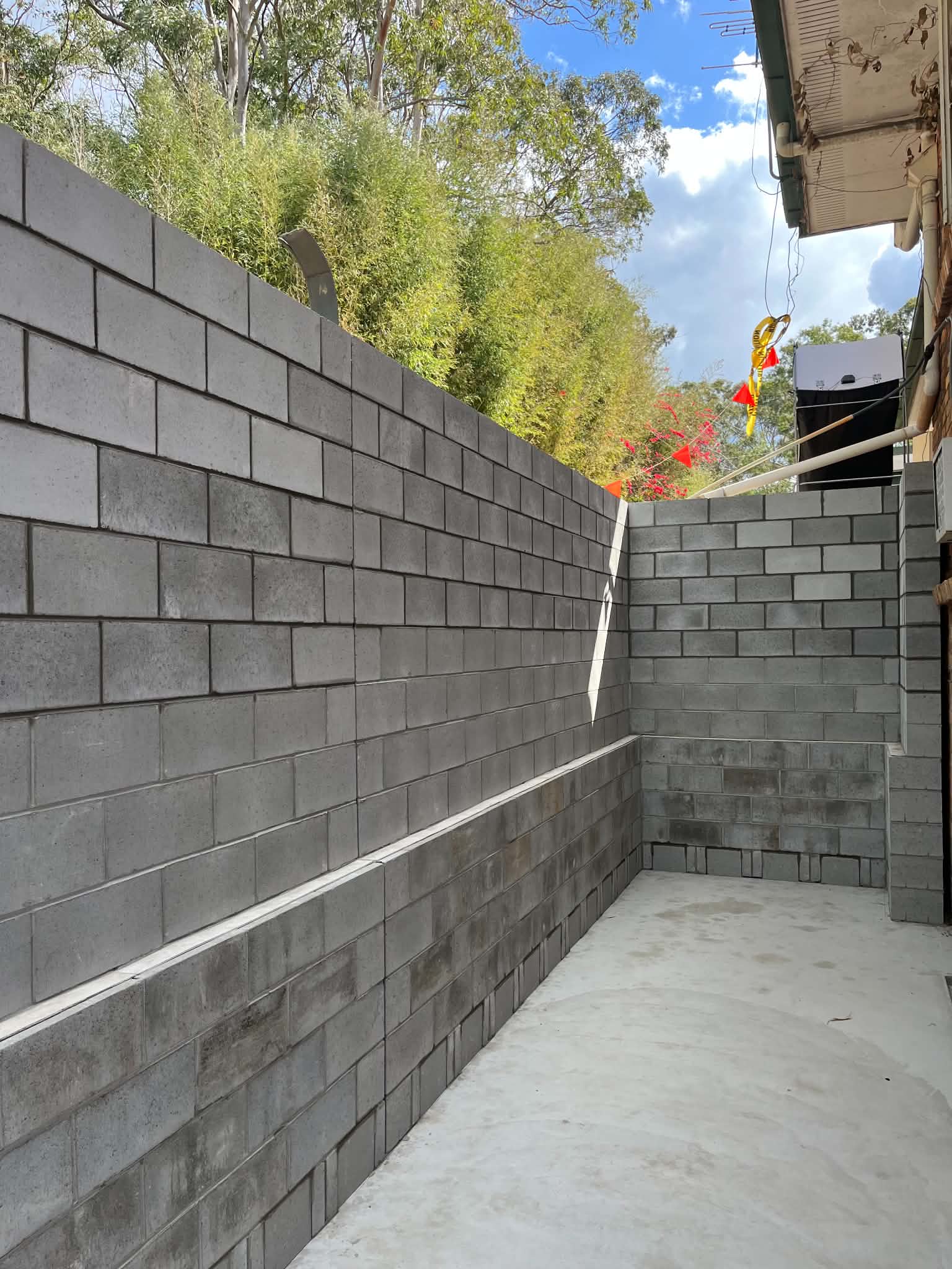 Tall grey block retaining wall stepping down beside a paved area