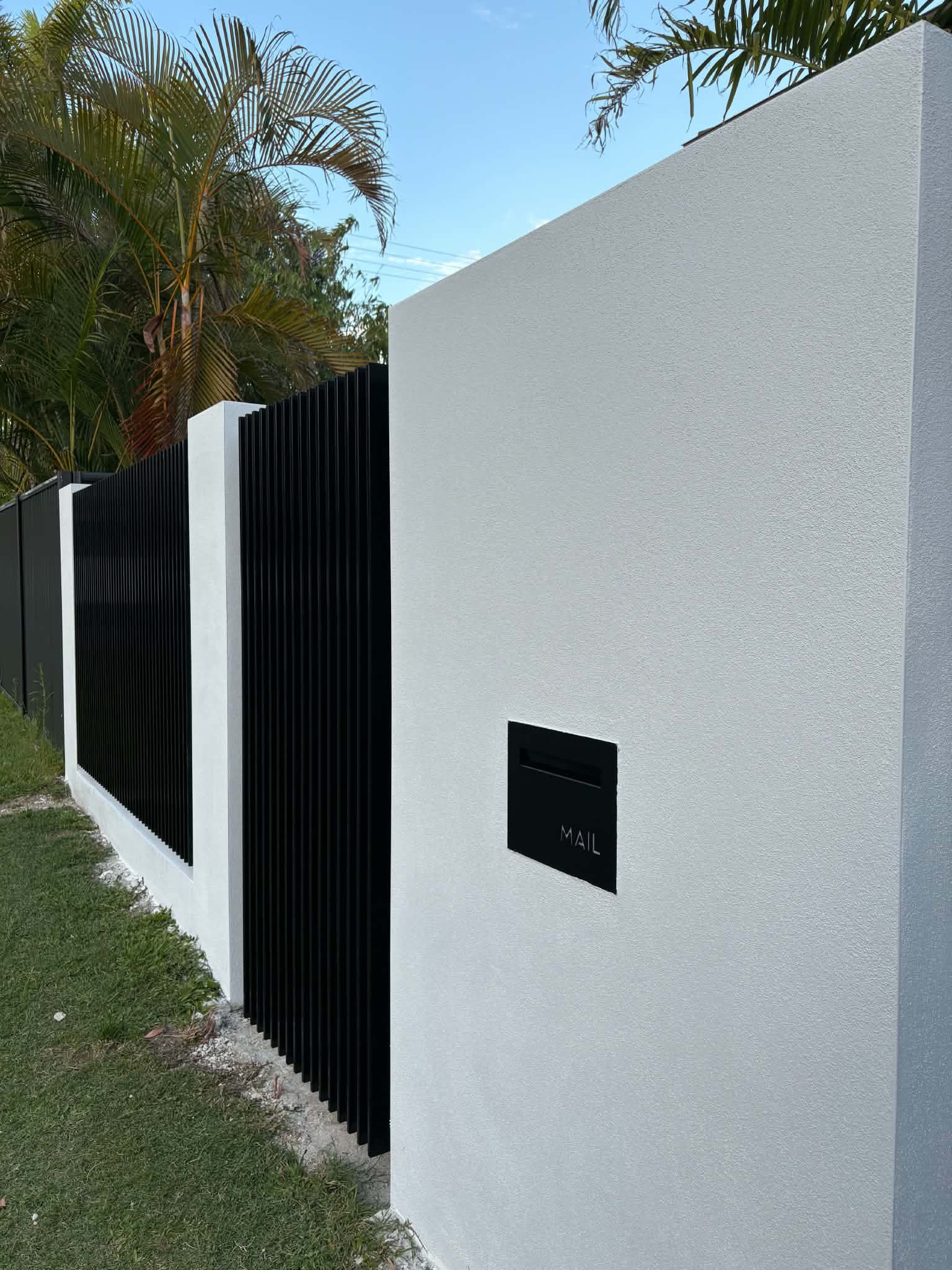 White rendered block fence pier with a black mailbox beside vertical black fence panels