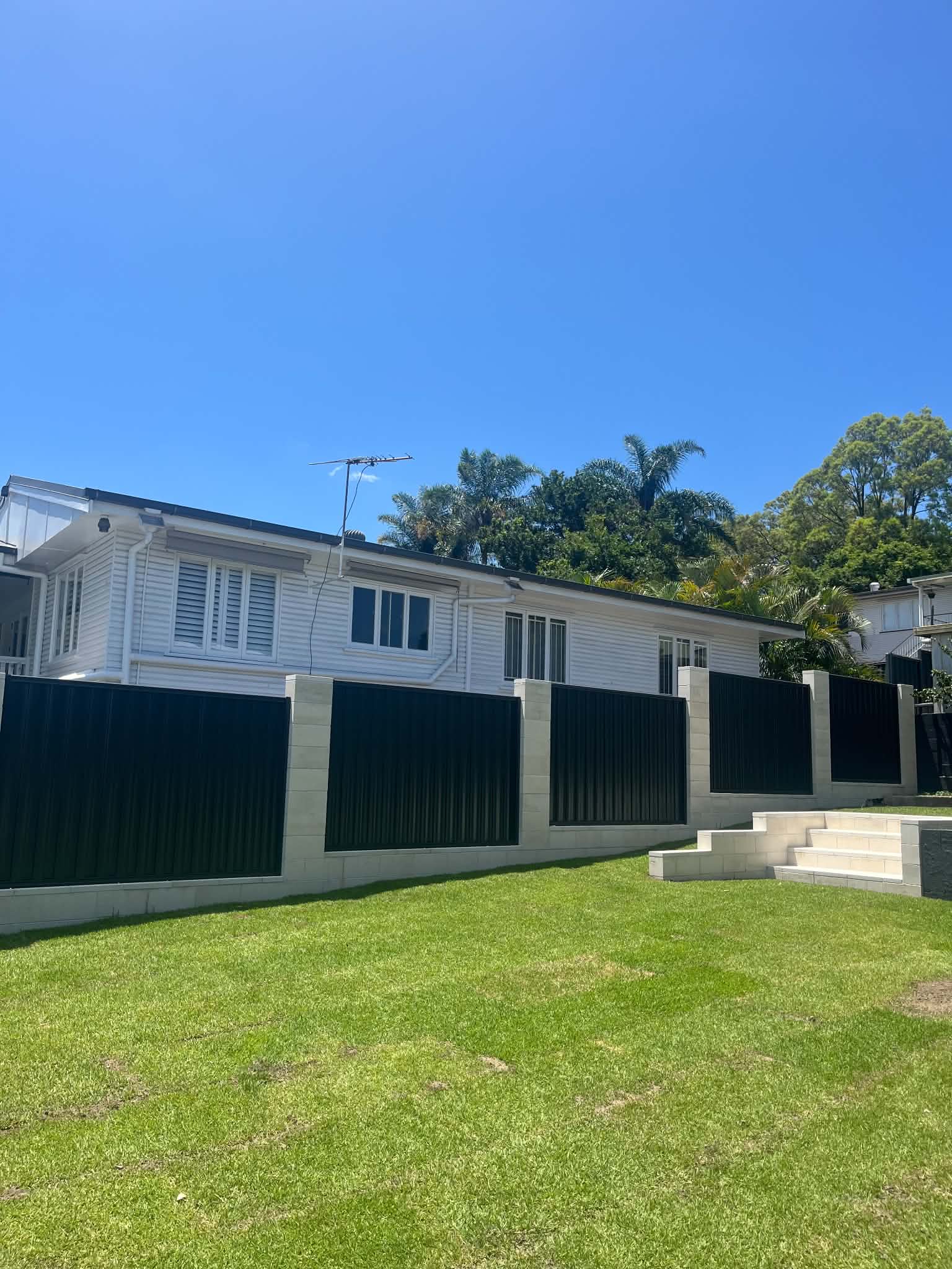 Light block retaining wall beneath a dark-panel fence and white home